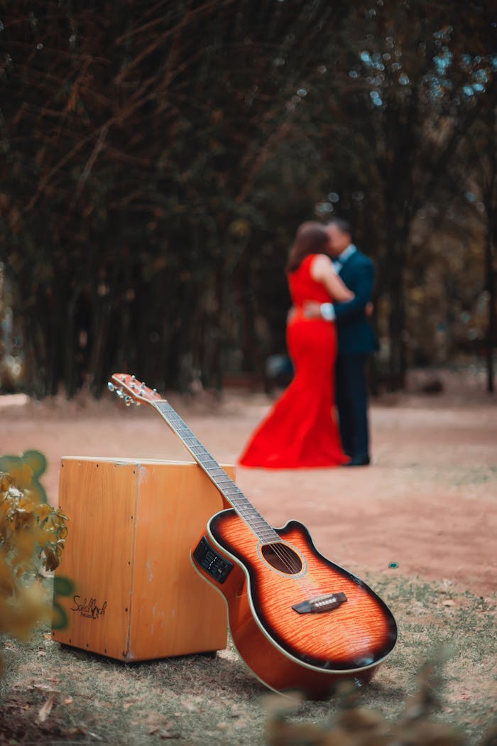 A couple embraces romantically outdoors with a guitar in focus.